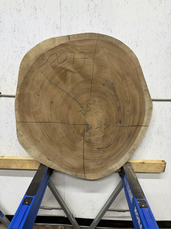 Round Parota live edge wood slab with a central cutout, leaning against a white brick wall on a wooden floor.

38x35