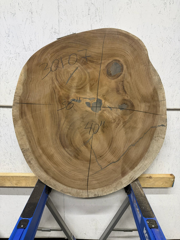 Round Parota live edge wood slab with a central cutout, leaning against a white brick wall on a wooden floor.

36x40