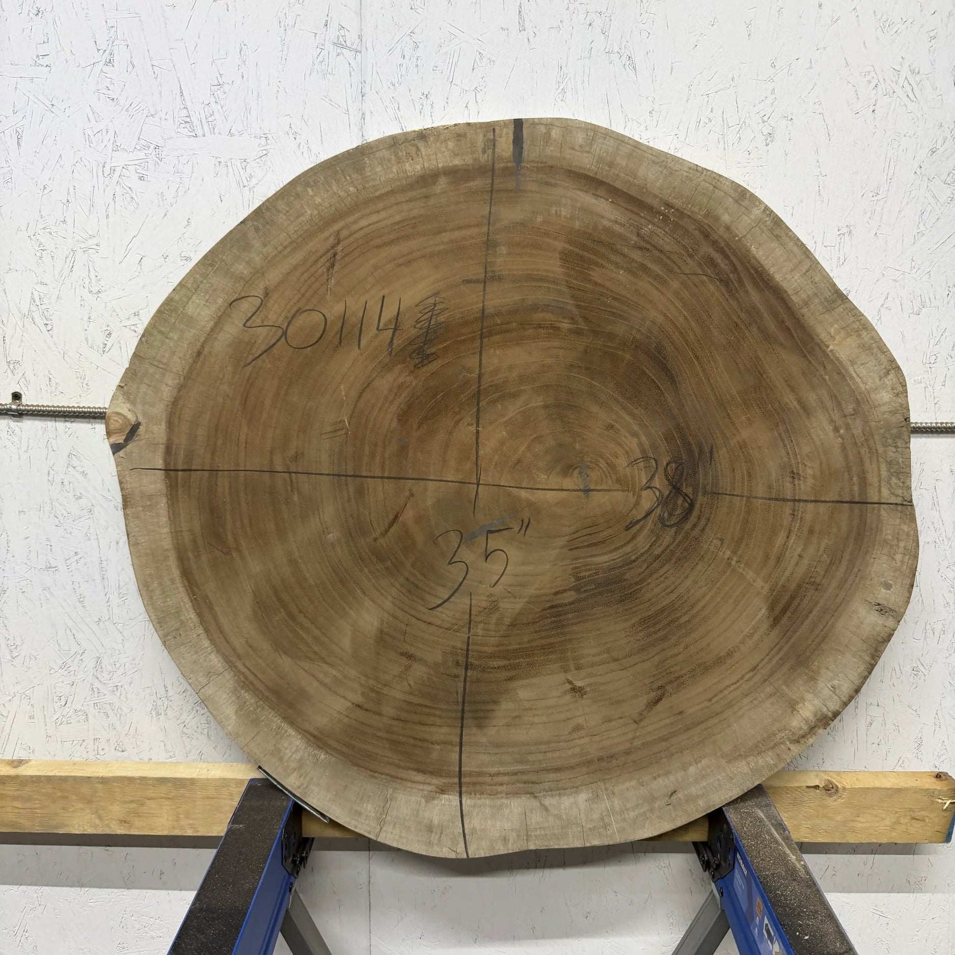 Round Parota live edge wood slab with a central cutout, leaning against a white brick wall on a wooden floor.

35x38